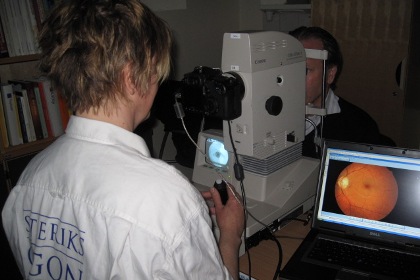 Patienten vilar sin haka i en undersökningsapparat medan ögonsjuksköterskan tar ögonbottenbilderna. Ett foto av en näthinna med dess blodkärl syns på en datorskärm