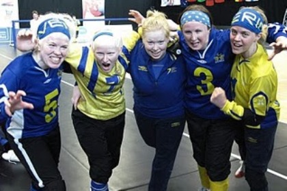 Svenska damlandslaget i Goalball, i blåa och gula tröjor, håller om varandra och skriker mot kameran.