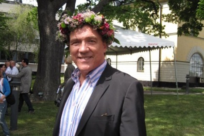 Christer Sjögren har vit- och blårandig skjorta och mörk kavaj. På huvudet bär han en blomsterkrans som täcker det kortklippta håret.