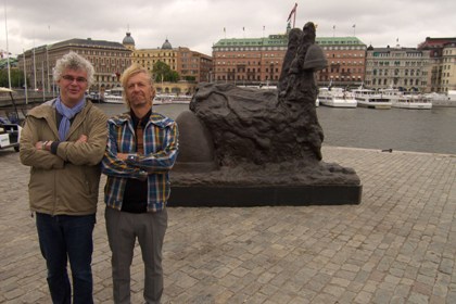 Konstnär och konstchef framför mörkgrå skulptur av smältande kyrka.