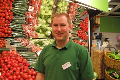 Butikschef Johan Beckman framför grönsakskylen på Coop Konsum. Han har en grön pikétröja och kort blont hår.