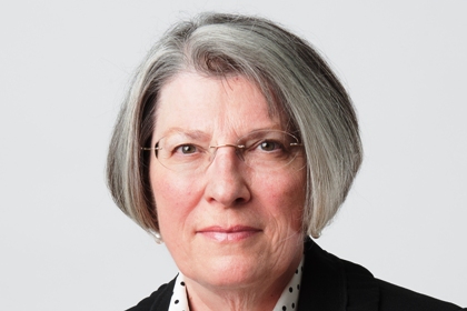 Adriana Lender har en grå page. Hon bär glasögon och en svart kavaj.