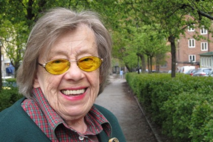Margareta Fromholtz  ordf. SRF Lidingö har grått kortklippt hår glasögon, med gula glas, en grön tröja och en rödrutig skjorta öppen i halsen.