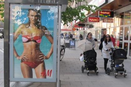 Bild på en annonspelare med baddräktsreklam och två föräldrar med barnvagn på Götgatan.