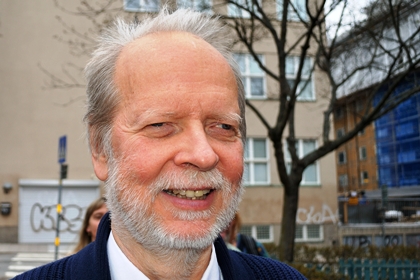 Kaj Nordquist har gråvitt hår och skägg. Han är klädd i vit skjorta, mörkblå kofta och han ler.