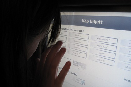 Sofia Naesström står med ansiktet tätt intill skärmen på SJ.s biljettautomat och försöker läsa texten.